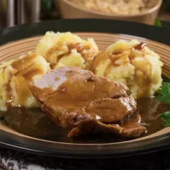 Pyszna karkówka w sosie podana z purée ziemniaczanym i gałązką natki pietruszki.