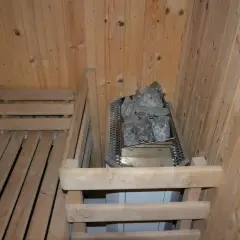 Drewniana sauna w piwnicy, z kamieniami na piecu i ławkami.