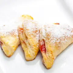 Trójkątne ciasteczka z ciasta francuskiego z dżemem, posypane cukrem pudrem. Idealne, gdy zastanawiasz się, co zrobić z ciasta francuskiego na szybką przekąskę.