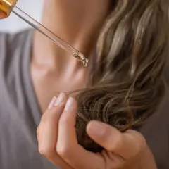 Una gota de aceite de aguacate para el pelo cae de un gotero sobre un mechón de cabello.