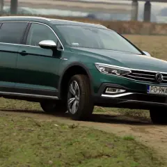 Zielony Passat Alltrack pokonuje piaszczystą drogę wśród traw.