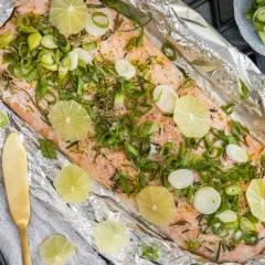 Lachsfilet in Alufolie gegrillt, garniert mit Limettenscheiben und Frühlingszwiebeln. Ein köstliches Gericht, das auf dem Grill zubereitet wird.