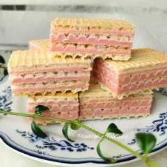Słodkie wafle z mlekiem w proszku, przełożone różowym kremem, ułożone na talerzyku z niebieskimi wzorami.