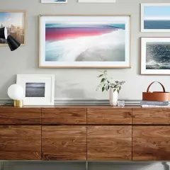 Ein moderner Wohnzimmerschrank aus Holz, der Kunstwerke und einen stilvollen Lampenständer präsentiert. Der große Bilderrahmen in der Mitte könnte einen **Fernseher verstecken**.