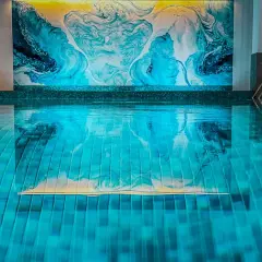 Relaks w nowoczesnym spa pod Poznaniem. Błękitna woda basenu odbija abstrakcyjną, turkusowo-żółtą mozaikę na ścianie.