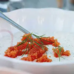 En skål med klassisk romsås, toppad med orange rom och dillkvistar. En sked vilar i skålen.