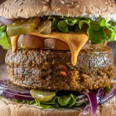 Deliciosa hamburguesa vegana con queso derretido, lechuga fresca, pepinillos y cebolla morada.