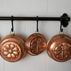 Cuencos de cobre decorados cuelgan de una barra. Aprende como limpiar cobre para que brillen así.