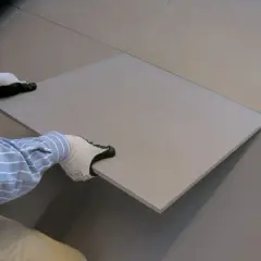 Mani guantate che posizionano una piastrella grigia su un pavimento, completando il lavoro di incollare piastrelle.