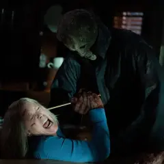 Michael Myers w masce i czarnym płaszczu trzyma nóż nad krzyczącą Laurie Strode. To przerażający halloweenowy finał.