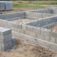Fundament domu powstaje z pustaków. Bloczek budowlany tworzy solidne ściany fundamentowe, a na placu budowy widać zapas materiału.