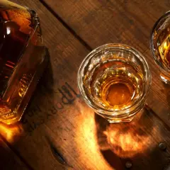 Butelka i dwa kieliszki bursztynowego trunku na drewnianym blacie. Zastanawiasz się, czym się różni koniak od whisky?
