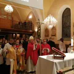Biskup w czerwonej szacie, który jest szafarzem bierzmowania, błogosławi wiernych w kościele.