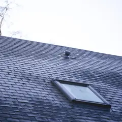Dach pokryty ciemną dachówką betonową płaską, z widocznym oknem dachowym i kominkiem wentylacyjnym.
