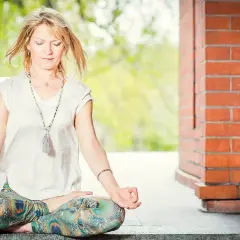 Kobieta w pozycji lotosu praktykuje jogę kundalini, z zamkniętymi oczami i dłońmi w mudrze.