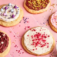 Bunte, verzierte Kekse, darunter ein mit weißer Creme und roten Krümeln bestreuter **crumble cookie**.