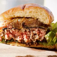 Przekrojony, soczysty burger z karmelizowaną cebulą i sałatą na desce.