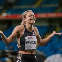 Uśmiechnięta Klaudia Wojtunik z rozłożonymi rękami na stadionie, celebrująca sukces.