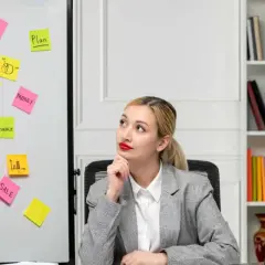 Kobieta zastanawia się nad strategią marketingową. Na tablicy karteczki z hasłami: "TEAM", "PRODUCT", "SALE", "DESIGN", "MONEY", "FINANCE", "PLAN".