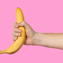 Dłoń trzyma banana na różowym tle. Facet robi sobie dobrze, używając owocu.