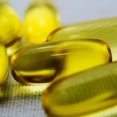 Kilka żółtych kapsułek z płynem, zawierających cenne kwasy omega 3, leży na białej powierzchni.