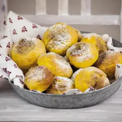 En skål med gyllene julgodis med saffran, pudrade med florsocker, på en duk med mönster.