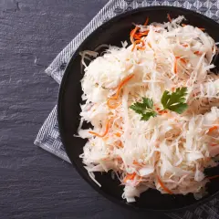 Ein Teller mit traditionellem Sauerkraut-Rezept, garniert mit Petersilie und Karottenstreifen, auf dunklem Stein serviert.