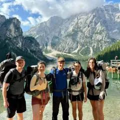 Cinco excursionistas sonríen junto a un lago turquesa con imponentes montañas de **Alta Ribagorza** al fondo.