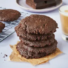 Ein Stapel saftiger brownie cookies, daneben ein Glas Latte Macchiato und ein Teller mit Schokoladenstücken.