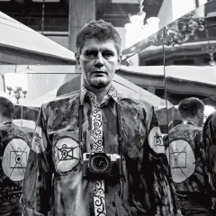 Krzysztof Miller w lustrzanym odbiciu, z aparatem na szyi, w koszuli z motywem oka.