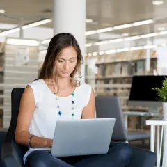 Kobieta siedzi w bibliotece, ucząc się, jak założyć PUE ZUS na laptopie.