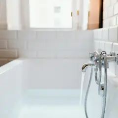 Woda leje się do wanny, a chromowana bateria przy białej, kafelkowej ścianie zapewnia idealne uszczelnienie wanny przy ścianie.