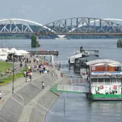 Toruń: Wisła, bulwar z ludźmi, restauracja na wodzie i mosty w tle.