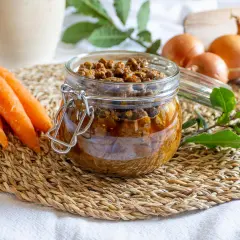 Un vasetto di vetro pieno di saporito ragù di anatra, con carote e cipolle sullo sfondo.
