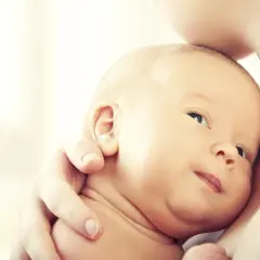 Noworodek wtulony w ramię dorosłego, z widoczną twarzą i uchem.