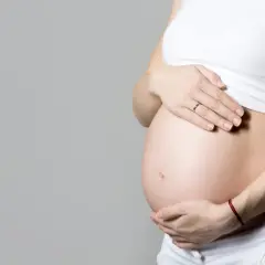 Ciężarna kobieta trzyma dłonie na brzuchu. Temat: umowa na zastępstwo a ciąża.