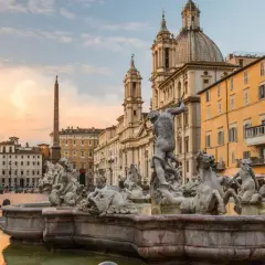 Fontana dei Quattro Fiumi a Piazza Navona, con l'obelisco e la chiesa di Sant'Agnese in Agone sullo sfondo, al tramonto.