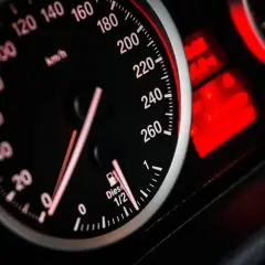 Zbliżenie na deskę rozdzielczą samochodu: prędkościomierz pokazuje 80 km/h, a obok wskaźnik paliwa wskazuje prawie pełny bak.