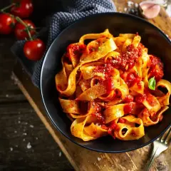 Pappardelle z sosem pomidorowym, świeże pomidory i bazylia. Pyszne dania z pomidorów na drewnianym blacie.