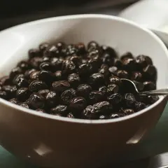 Un cuenco blanco lleno de aceitunas negras brillantes, perfecto para tus recetas con aceitunas negras.