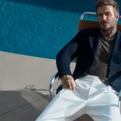 David Beckham style: en man i mörk kavaj och vita byxor sitter vid en pool.