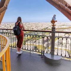 En kvinna med ryggsäck njuter av utsikten över Paris från Eiffeltornet. Hon undrar nog hur många trappsteg har Eiffeltornet.
