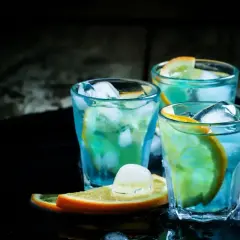 Trzy orzeźwiające drinki z blue curacao, ozdobione plasterkami pomarańczy i kostkami lodu, kuszą swoim tropikalnym kolorem.