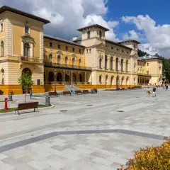 Plac przed zabytkowym sanatorium. Ludzie spacerują, odpoczywają na ławkach. Może to miejsce, gdzie czekają na nowe zasady wyjazdu do sanatorium na NFZ.