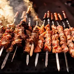 Rader av saftiga köttspett grillas över glöd. Röken stiger och doften lovar något gott att grilla.