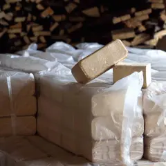 Stosy opakowanego, taniego brykietu drzewnego w magazynie. W tle widać drewno opałowe.