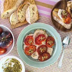 Tomates italianos asados sobre una crema suave, acompañados de pan rústico y tomates frescos.