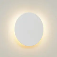 Un aplique redondo de pared blanco emite una luz cálida y difusa, creando un ambiente acogedor.