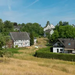 Fachwerkhäuser säumen den malerischen fachwerkweg Ruppichteroth, eingebettet in grüne Hügel unter blauem Himmel.