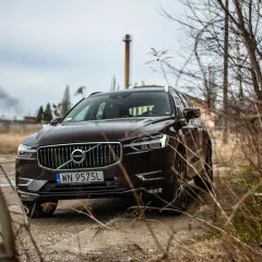 Brązowe Volvo XC60 T5 na tle opuszczonej fabryki i suchych gałęzi.